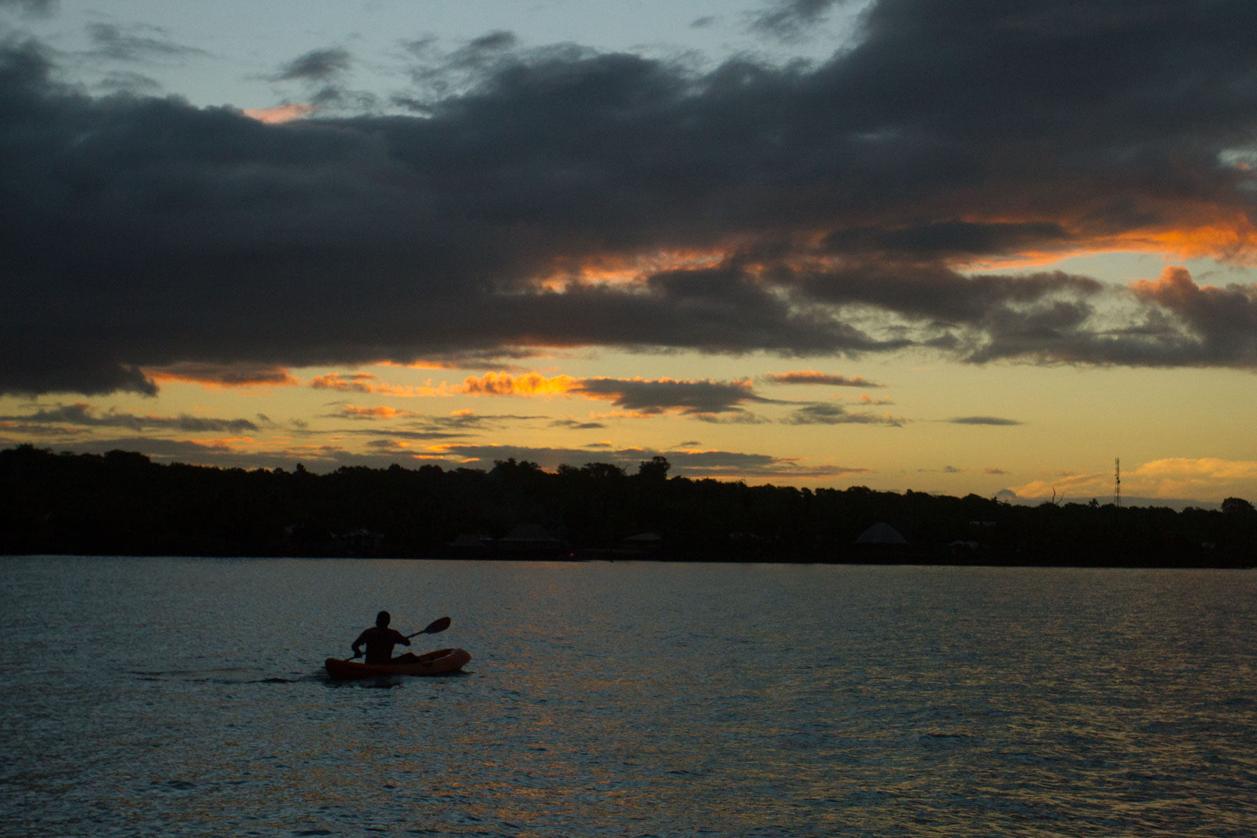 A man paddles to a nearby village as the sun sets