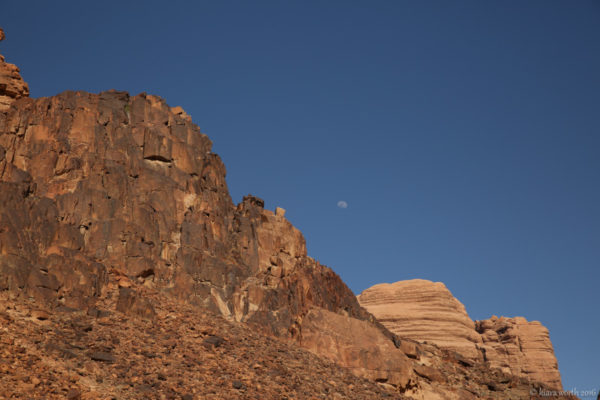 The half moon peeks out from behind the mountains.