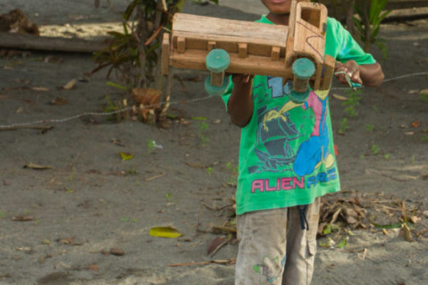 A young boy stands proudly with his wooden toy car, the wheels made from plastic bottle caps.