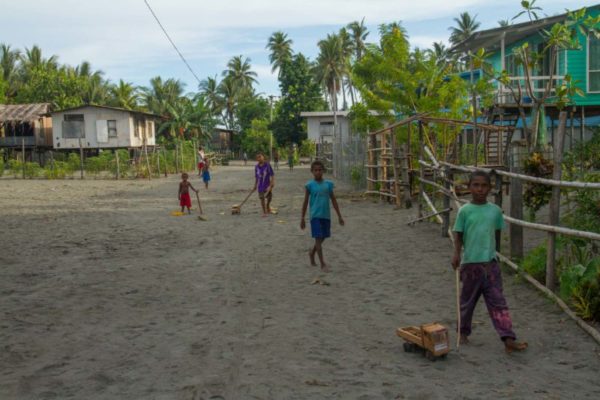 A group of boys play with wooden toy cars on the sands streets of Iokea village.