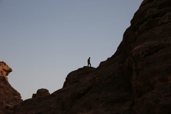 A man is silhouetted against the sky while climbing on top of the rocks.