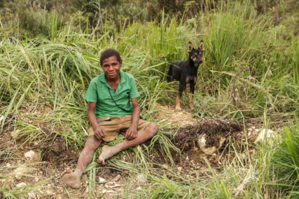 Mendi, Southern Highlands Province, 2012. A boy and his dog sit along the side of the road.